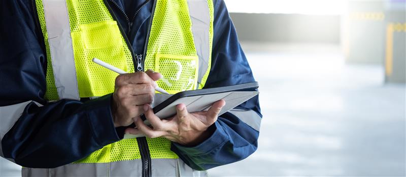 Ground crew or logistics worker in a high-visibility safety vest using a digital tablet outdoors.